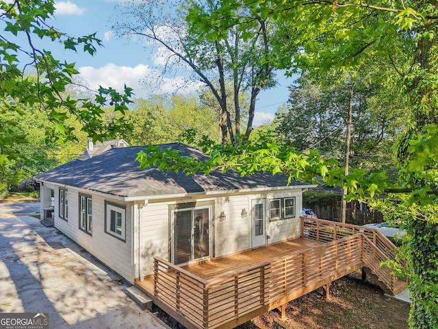back of house featuring a shingled roof, a wooden deck, and a chimney