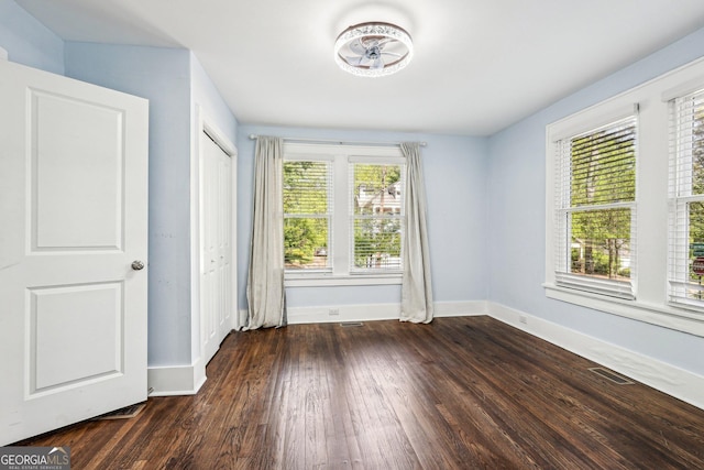 unfurnished bedroom with baseboards, dark wood-style floors, multiple windows, and visible vents