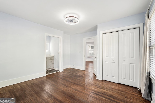 unfurnished bedroom with baseboards, dark wood-style flooring, ensuite bathroom, and a closet