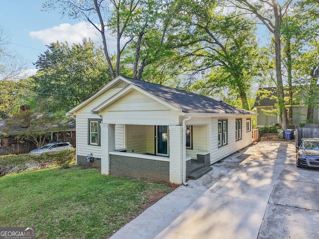 bungalow-style home with a porch, fence, driveway, and a front lawn