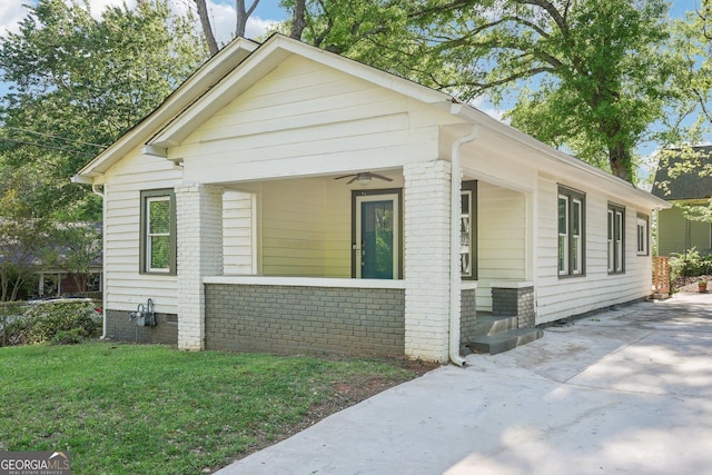 view of front of house with brick siding, a ceiling fan, driveway, and a front yard