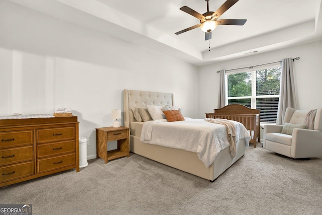 bedroom with light colored carpet, a raised ceiling, ceiling fan, and visible vents