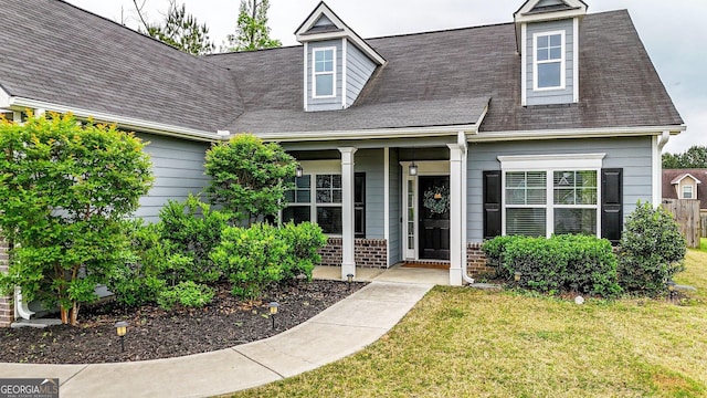 view of front of home with a porch, roof with shingles, and a front yard