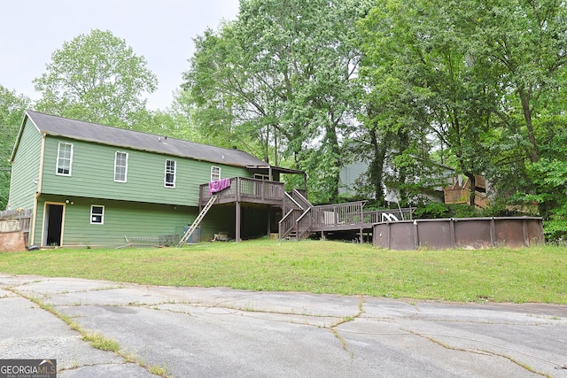 back of property with a lawn, an outdoor pool, stairs, and a wooden deck