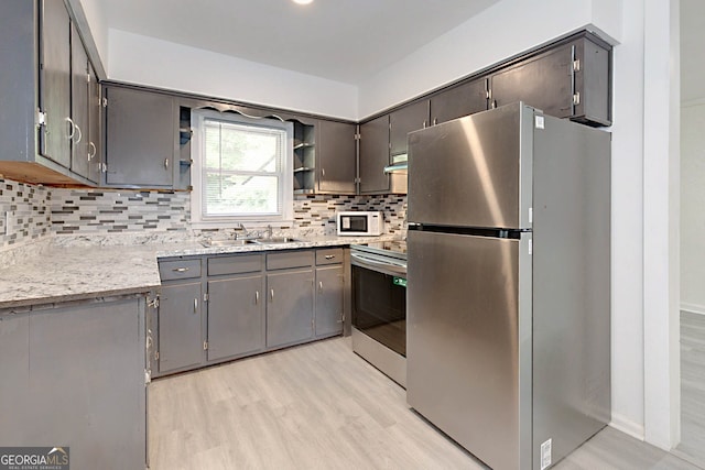 kitchen featuring a sink, stainless steel appliances, open shelves, light wood-type flooring, and tasteful backsplash