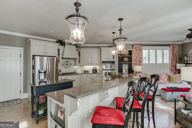 2930 Aquitania Ln, Cumming, GA 30040 - kitchen with crown molding, a kitchen island with sink, light wood-style flooring, and appliances with stainless steel finishes