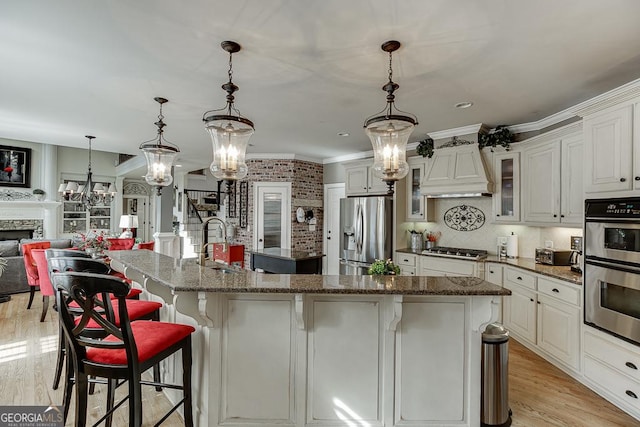 2930 Aquitania Ln, Cumming, GA 30040 - kitchen with custom exhaust hood, light wood-style floors, appliances with stainless steel finishes, a sink, and a center island with sink