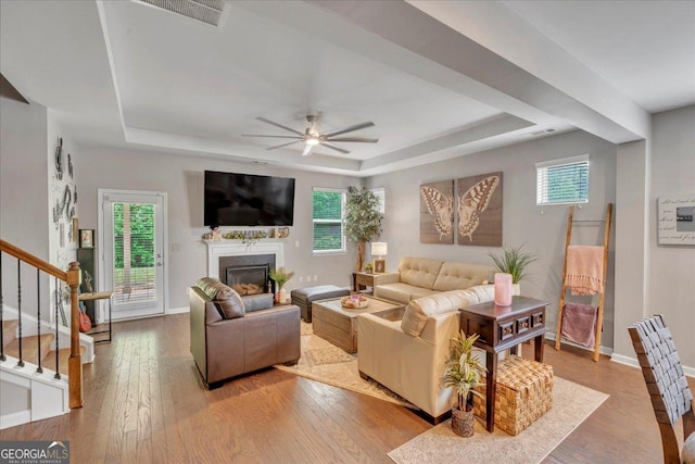 living area with light wood-type flooring, a raised ceiling, and a wealth of natural light