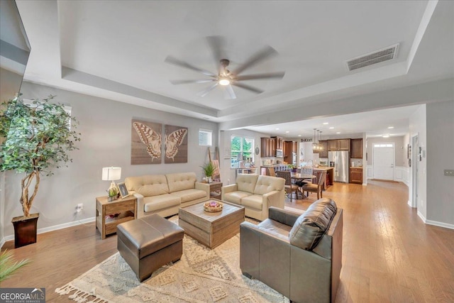 living room featuring a raised ceiling, visible vents, light wood-type flooring, and a ceiling fan