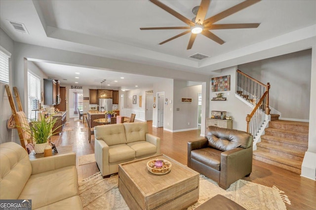 living area featuring light wood-style floors, ceiling fan, visible vents, and stairs