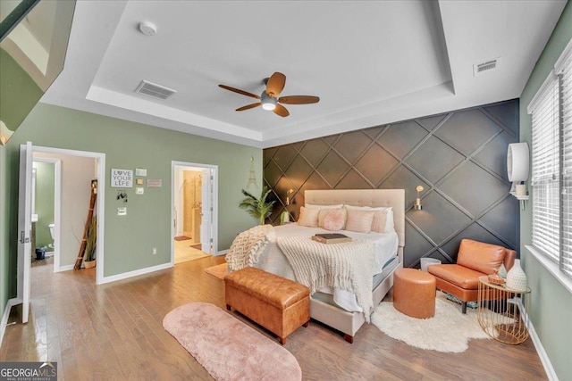bedroom featuring an accent wall, visible vents, baseboards, and a tray ceiling
