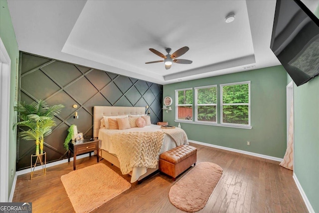 bedroom with an accent wall, a raised ceiling, ceiling fan, hardwood / wood-style floors, and baseboards