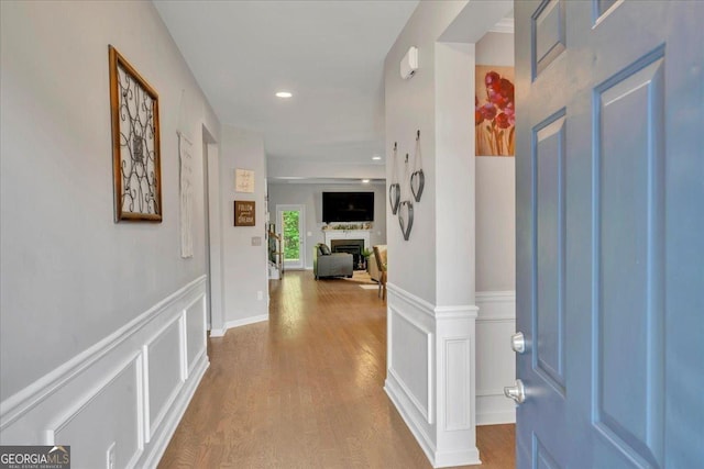 corridor with a decorative wall, wood finished floors, recessed lighting, and a wainscoted wall