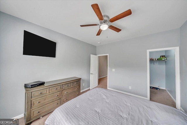 bedroom with a walk in closet, ceiling fan, light carpet, and baseboards