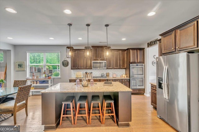 kitchen featuring light stone countertops, decorative backsplash, stainless steel appliances, and an island with sink