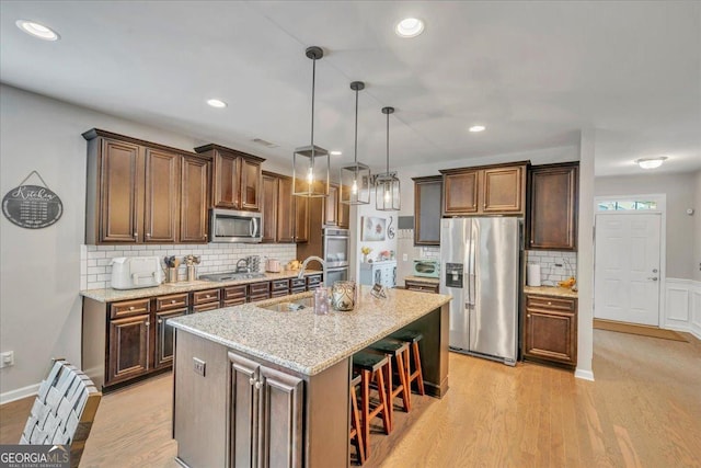 kitchen featuring light wood-style floors, appliances with stainless steel finishes, decorative backsplash, and a sink