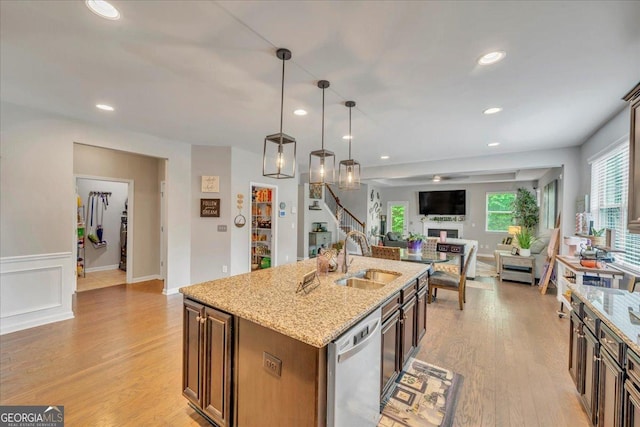 kitchen with light stone countertops, dishwasher, light wood finished floors, a sink, and open floor plan