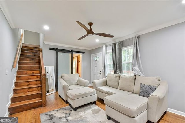 living room with stairway, a barn door, light wood-style floors, crown molding, and a ceiling fan