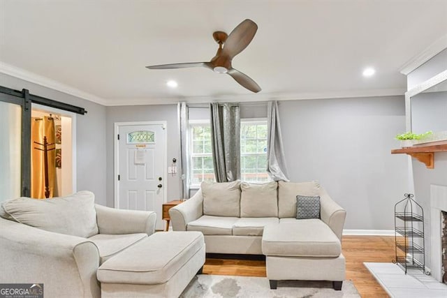 living room featuring a barn door, light wood-style floors, ornamental molding, ceiling fan, and a glass covered fireplace