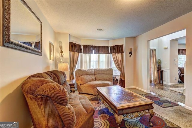 carpeted living room featuring visible vents, a wealth of natural light, and a textured ceiling