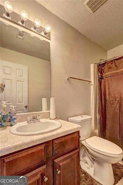 bathroom with toilet, a textured ceiling, visible vents, and vanity