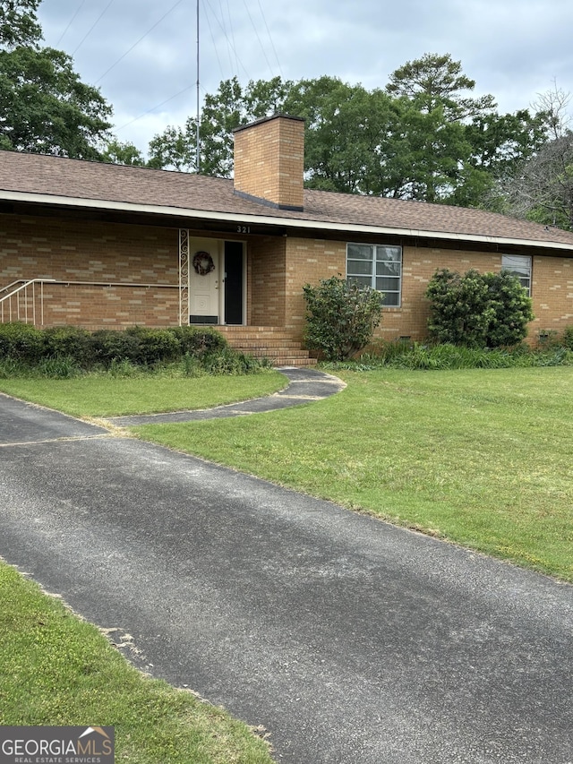 single story home with a chimney, brick siding, a shingled roof, and a front yard
