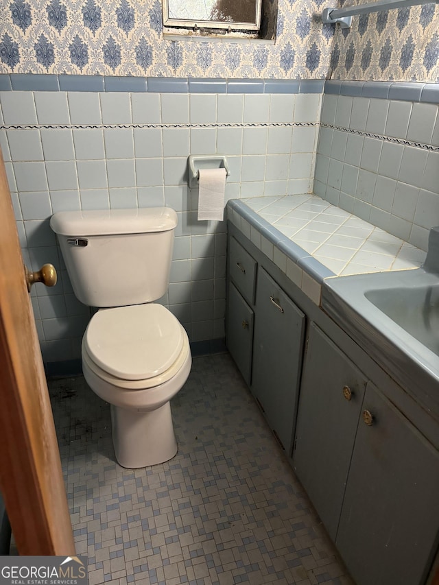 bathroom with vanity, tile patterned floors, toilet, a wainscoted wall, and wallpapered walls