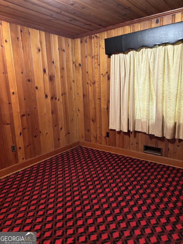 carpeted empty room featuring baseboards, wood walls, visible vents, and wood ceiling