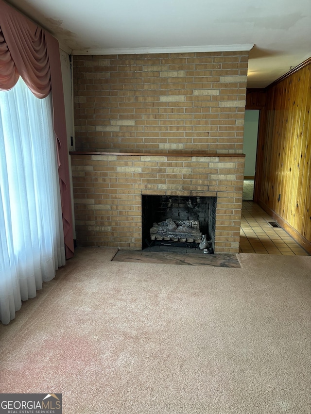 unfurnished living room with carpet floors, a brick fireplace, visible vents, wooden walls, and crown molding