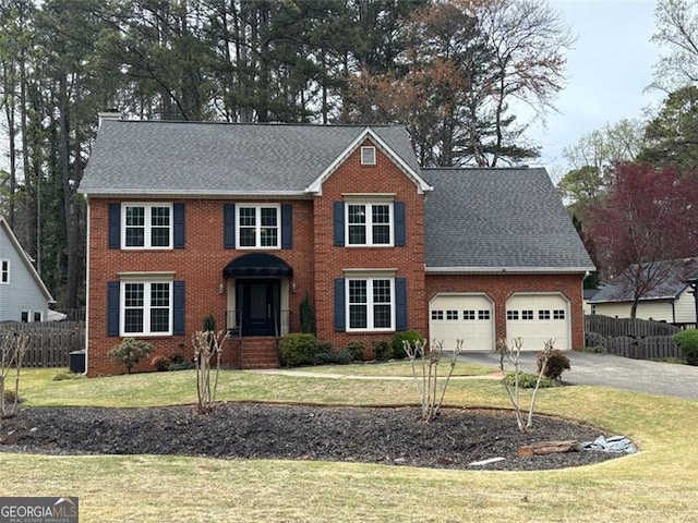 colonial house featuring fence, an attached garage, driveway, and a front yard