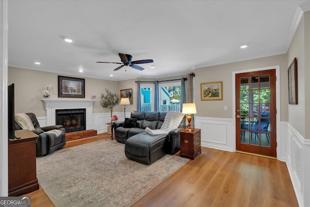 living area featuring a fireplace with raised hearth, ceiling fan, ornamental molding, and a wainscoted wall