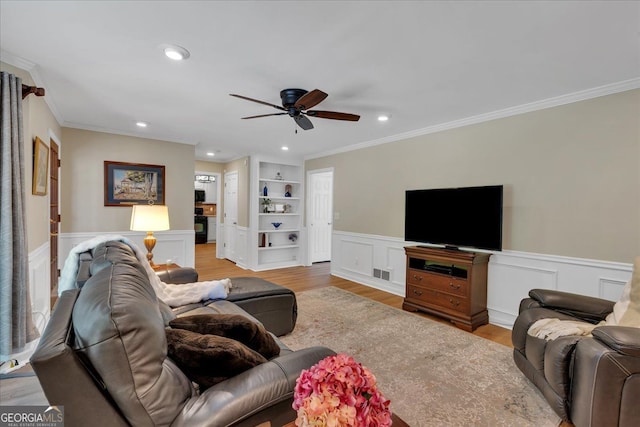 living area featuring visible vents, ornamental molding, built in features, ceiling fan, and light wood-type flooring