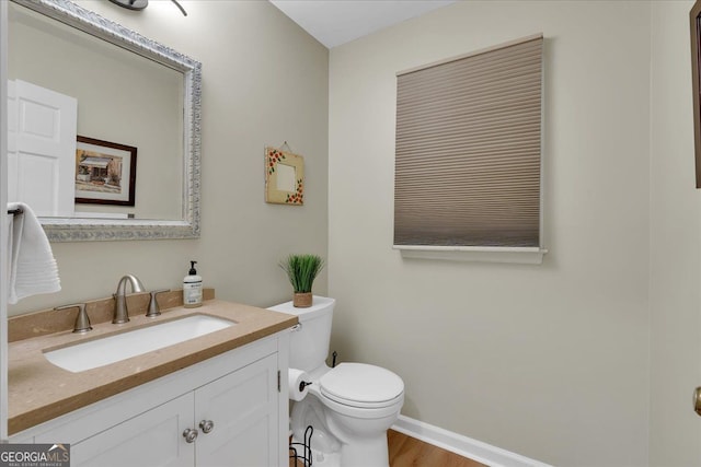 half bathroom featuring toilet, baseboards, wood finished floors, and vanity