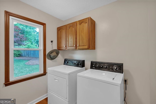 laundry area featuring washing machine and clothes dryer, a textured ceiling, baseboards, and cabinet space