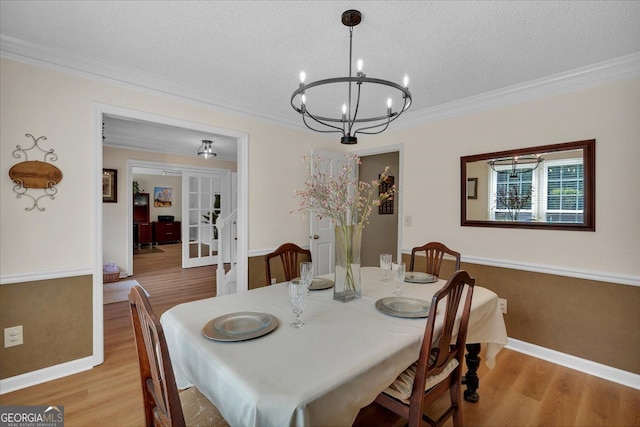 dining area with an inviting chandelier, ornamental molding, light wood finished floors, and a textured ceiling