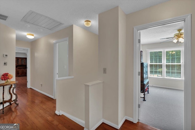 corridor featuring a textured ceiling, baseboards, an upstairs landing, wood finished floors, and visible vents