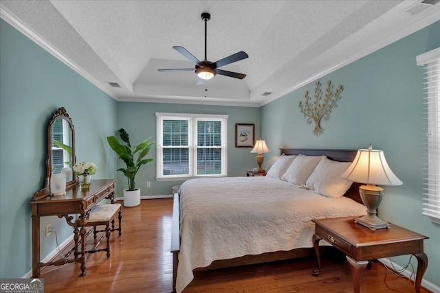 bedroom with crown molding, wood finished floors, baseboards, a textured ceiling, and a tray ceiling