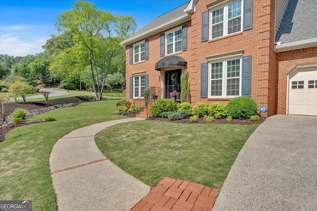 colonial home featuring a garage, aphalt driveway, a front yard, brick siding, and a shingled roof