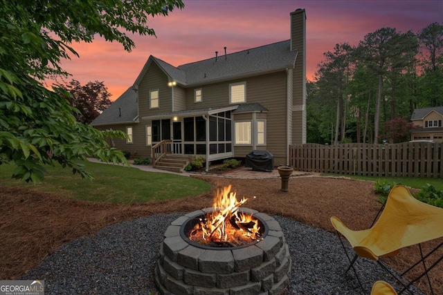 back of house with a chimney, a sunroom, fence, a yard, and a fire pit