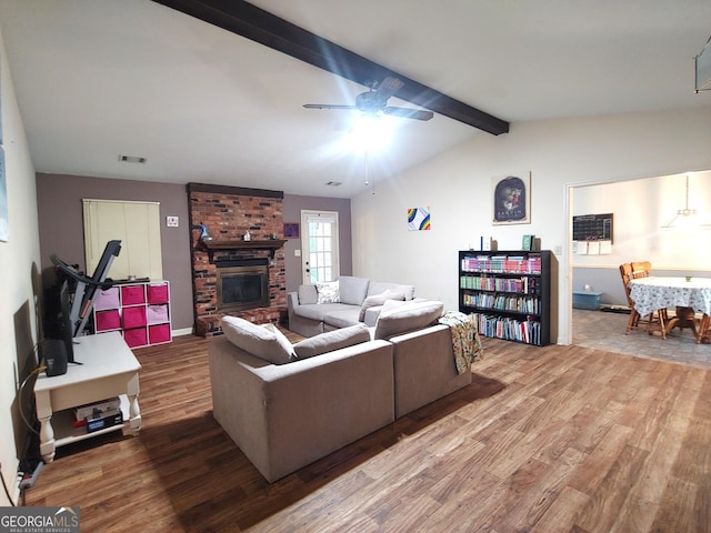 living room featuring visible vents, lofted ceiling with beams, a brick fireplace, wood finished floors, and a ceiling fan