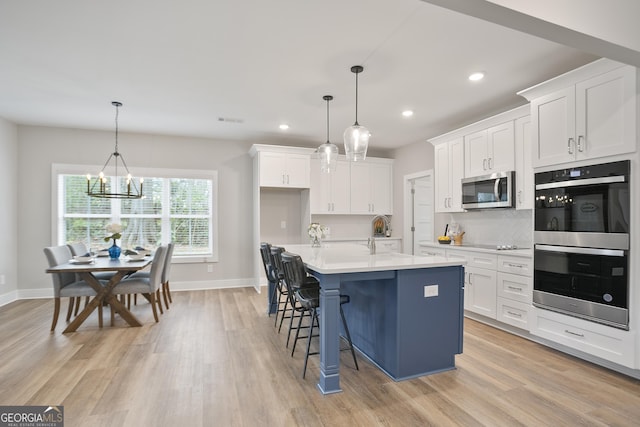 kitchen featuring light wood-style flooring, appliances with stainless steel finishes, white cabinets, a sink, and a notable chandelier