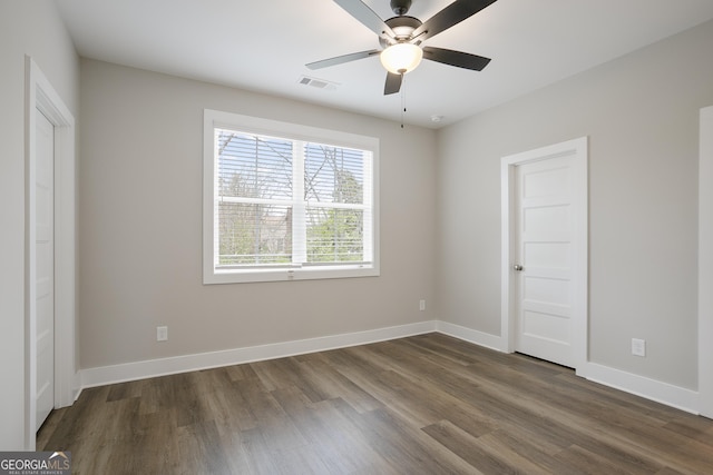 spare room with dark wood-style floors, visible vents, ceiling fan, and baseboards
