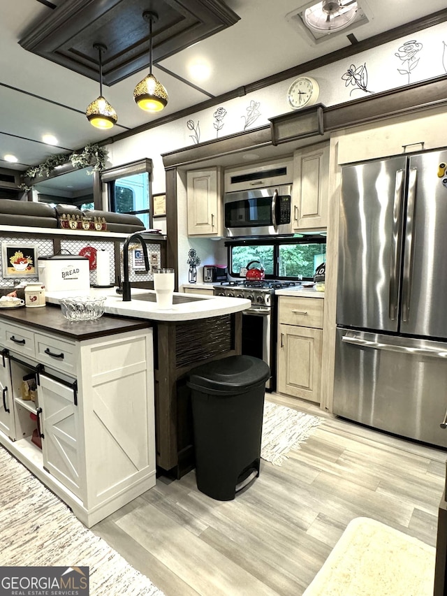 kitchen featuring an island with sink, light wood-style flooring, stainless steel appliances, a sink, and pendant lighting