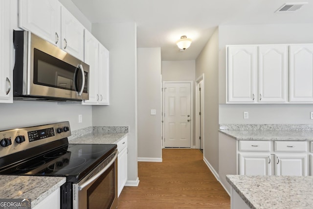 kitchen featuring appliances with stainless steel finishes, light wood-style flooring, white cabinetry, baseboards, and light stone countertops