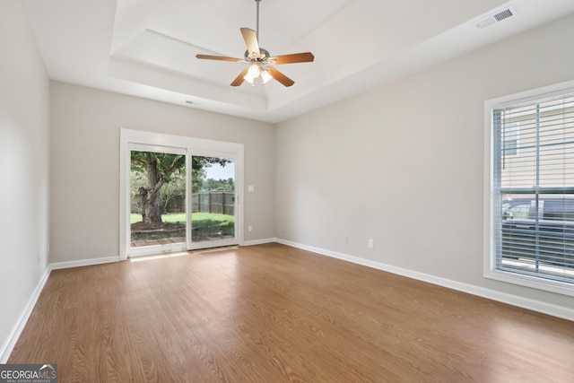 empty room featuring wood finished floors, a tray ceiling, baseboards, and ceiling fan