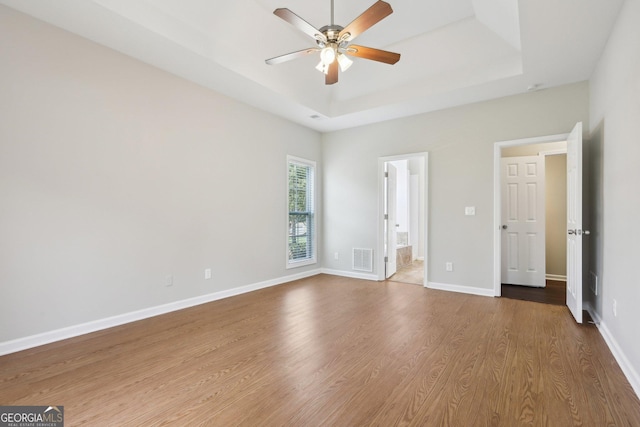 unfurnished bedroom with wood finished floors, baseboards, a raised ceiling, and a ceiling fan