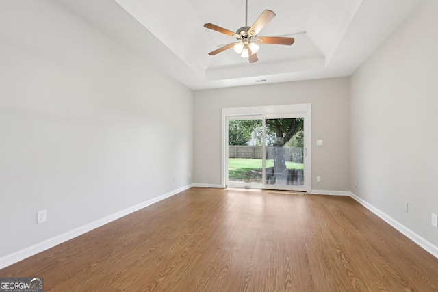 empty room featuring a raised ceiling, wood finished floors, ceiling fan, and baseboards
