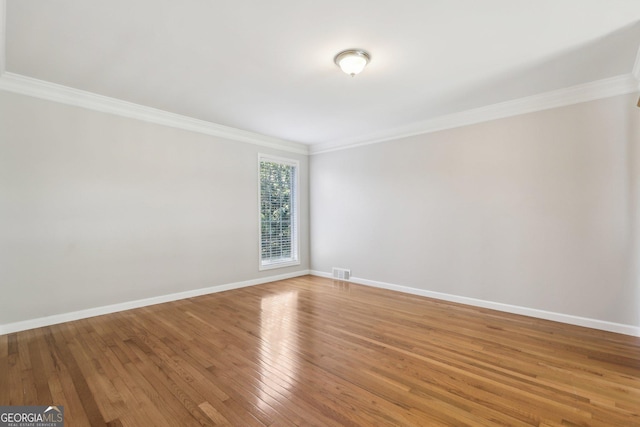 spare room with ornamental molding, baseboards, and light wood finished floors