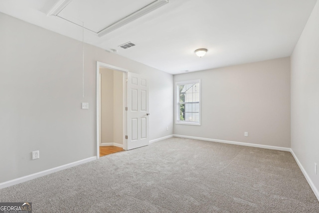 spare room with attic access, carpet, and baseboards