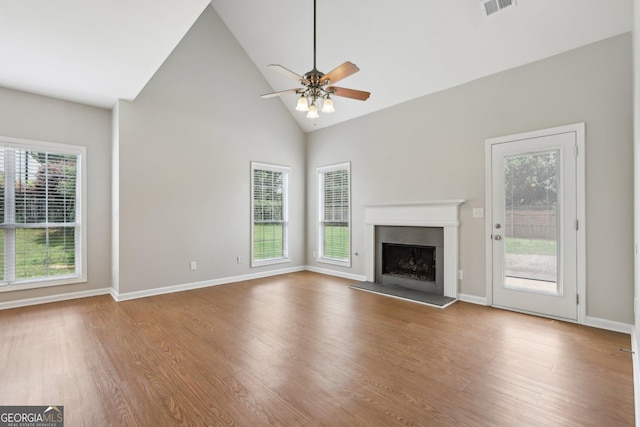 unfurnished living room with a fireplace with raised hearth, wood finished floors, high vaulted ceiling, a ceiling fan, and baseboards